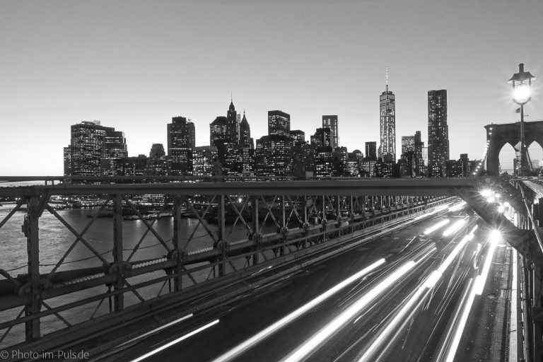 Schwarz-Weiß-Foto der Skyline von New York mit Lichtspuren auf der Brücke