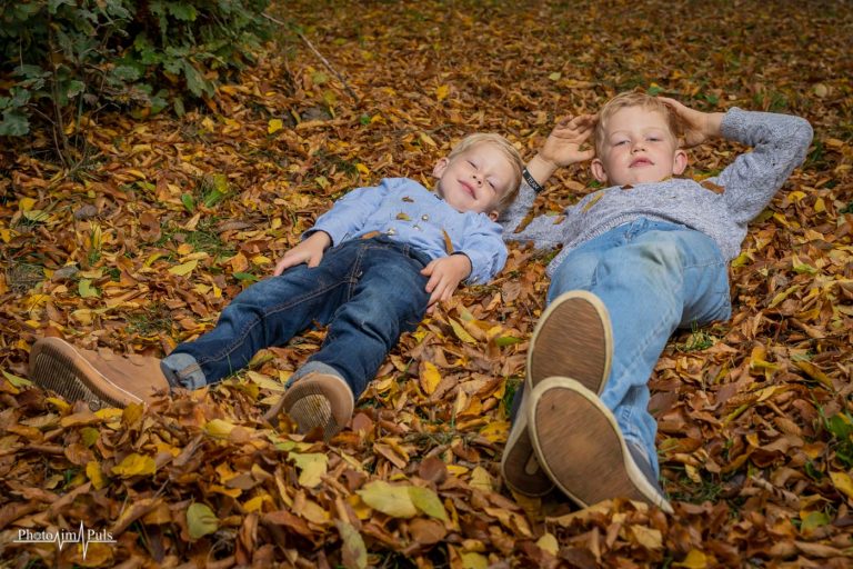 Zwei Kinder liegen lachend im Herbstlaub