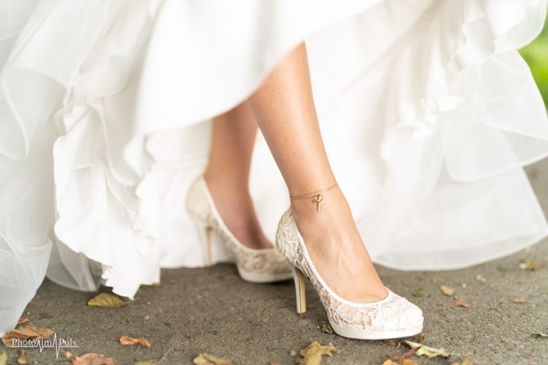 Detailaufnahme der Brautschuhe mit Spitze unter dem weißen Brautkleid