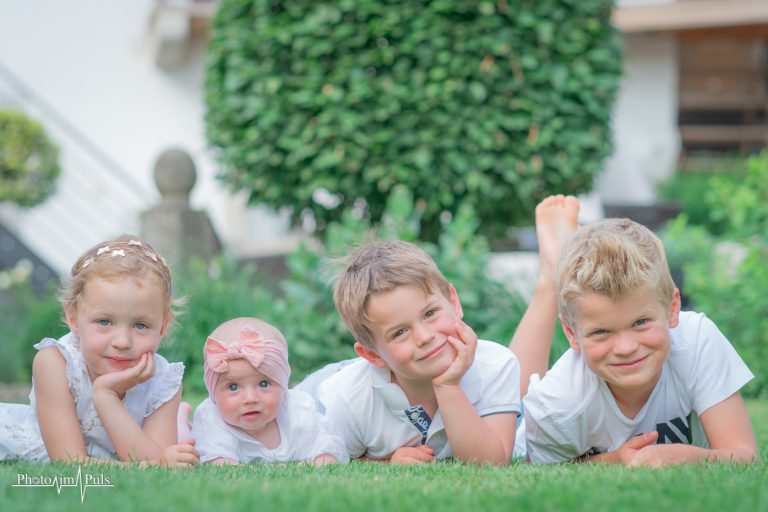 Vier Kinder liegen nebeneinander auf einer Wiese und lächeln in die Kamera