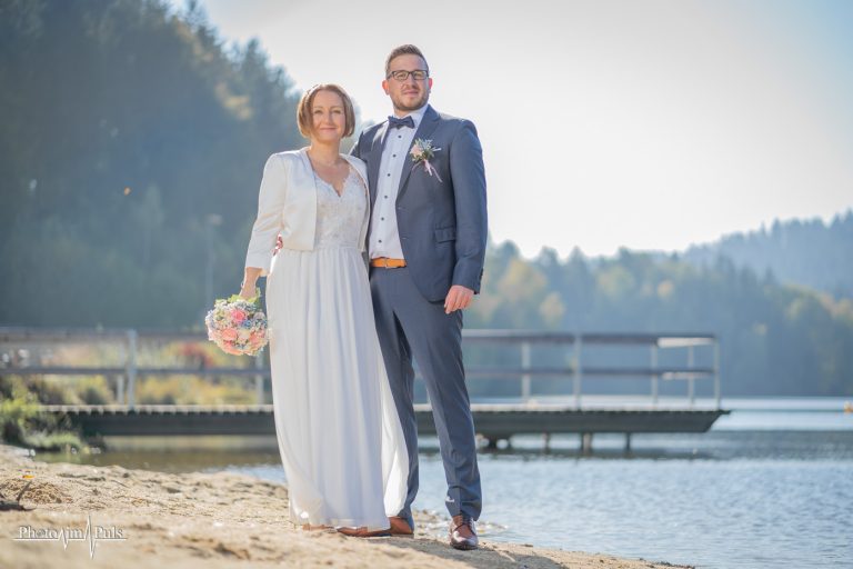 Brautpaar am Seeufer mit Bootssteg im Hintergrund