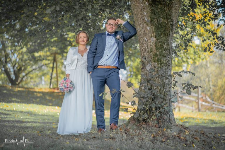 Brautpaar lehnt an einem Baum im Herbstlicht