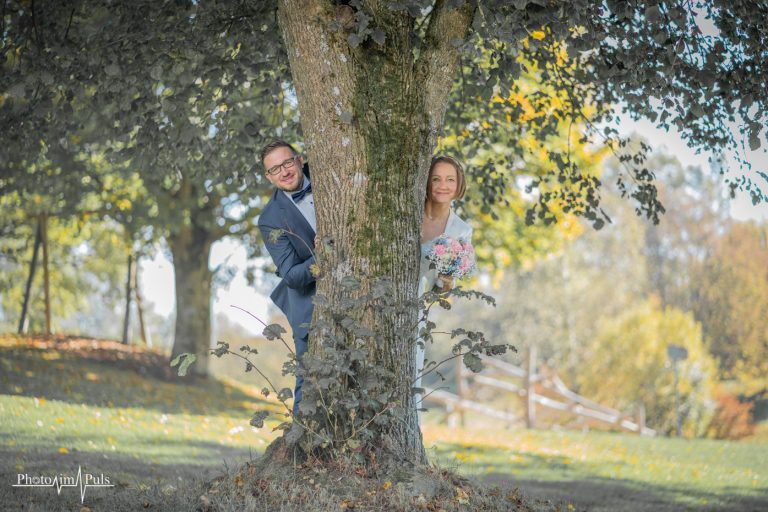 Brautpaar schaut hinter einem großen Baum hervor