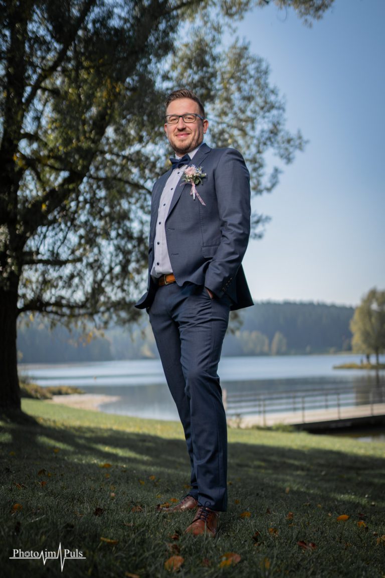 Bräutigam Marko lehnt an einem Baum am See