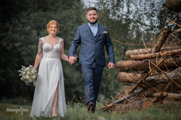 Christina und Jonny gehen Hand in Hand an gestapeltem Holz vorbei