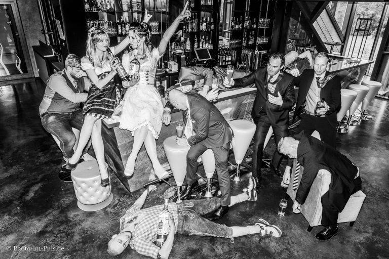 Schwarz-Weiß-Foto einer ausgelassen feiernden Hochzeitsgesellschaft an einer Bar