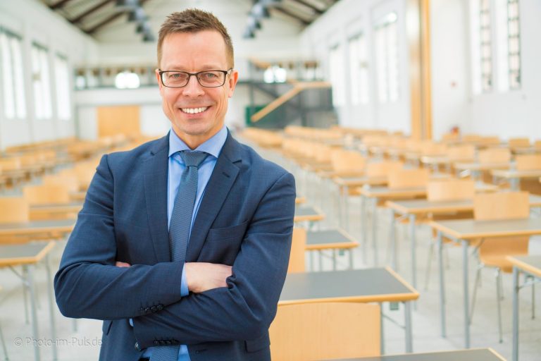 Mann im Anzug mit verschränkten Armen in einem Seminarraum
