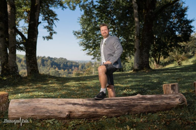 Johannes in Lederhose und Trachtenjanker auf dem Baumstamm